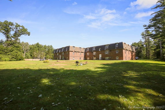 Front view of a two-story brick building with multiple dormer windows and a large lawn area.
