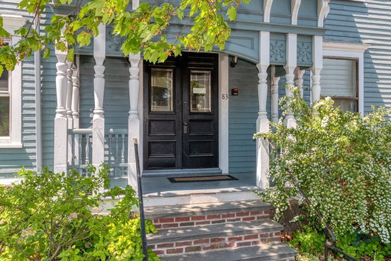 Front view of a house with ornate wooden columns and a dark colored front door.