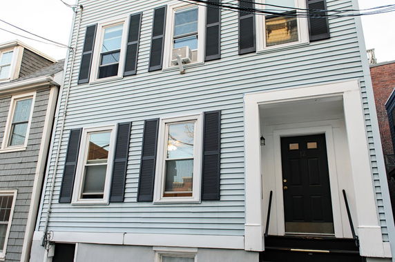 Front view of a multi-story house with blue siding and black shutters.