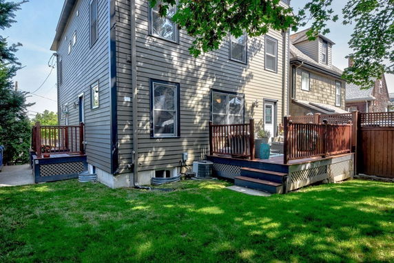 Rear view of a two-story house with wooden deck and fenced backyard.