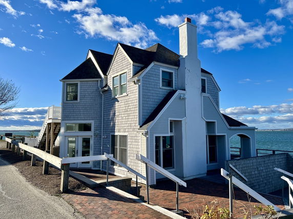 Front view of a two-story house with a chimney and an ocean backdrop.