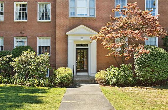 Front view of a brick multi-story building with a central entrance and surrounding greenery.