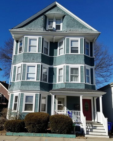 Front view of a multi-story house with green siding and a red door.