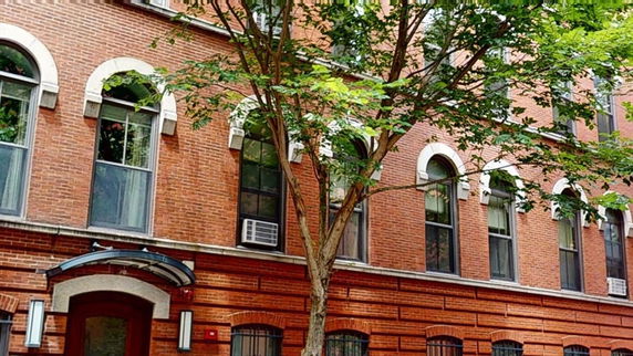 Front view of a multi-story brick building with arched windows and a glass canopy.