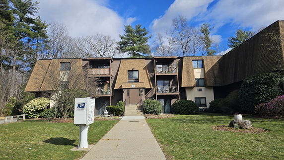 Front view of a multi-story residential building with balconies and a sloped roof.