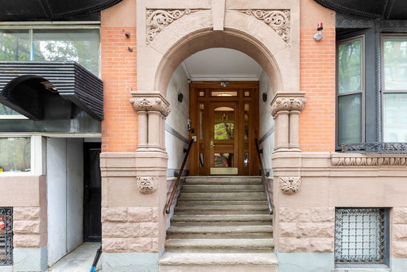 Front entrance of a building with ornate stonework and stairs leading up to a wooden door.