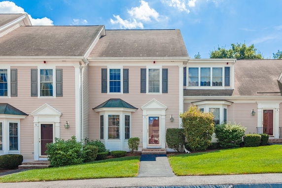 Front view of a two-story townhouse with light pink siding and decorative shutters.
