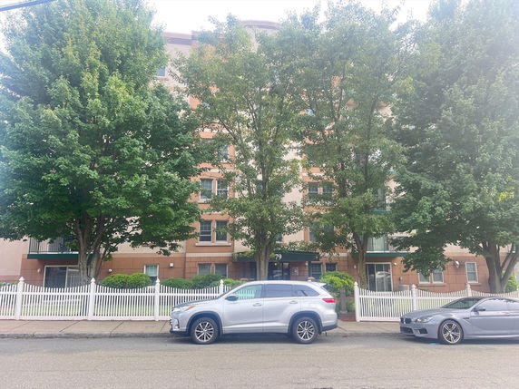 Front view of a multi-story building with a white fence and trees in front.