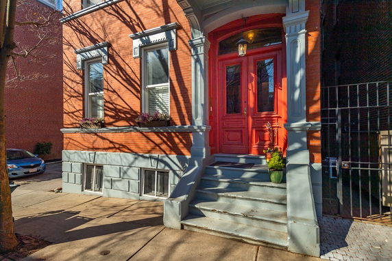 Front view of a brick house with a red front door and steps leading up to the entrance.