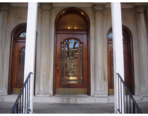 Front view of a building entrance with large wooden doors and ornate glass panels, flanked by stone columns.