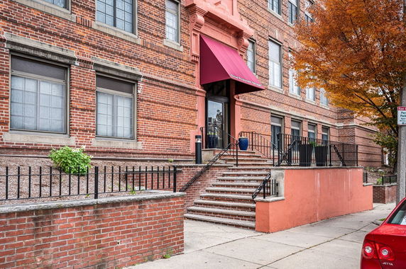 Front view of a brick building with red awning above the entrance and steps leading up.