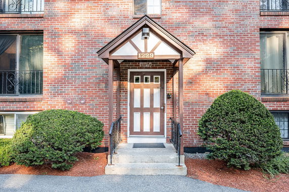 Front view of a brick building entrance with a covered doorway and stairs.