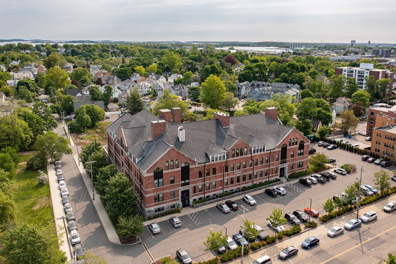 Aerial view of a large brick building surrounded by trees and residential houses.