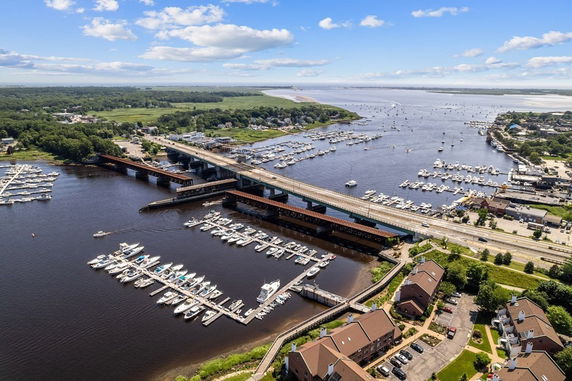 Aerial panoramic view of a river with multiple docks and boats, surrounded by residential buildings and greenery.