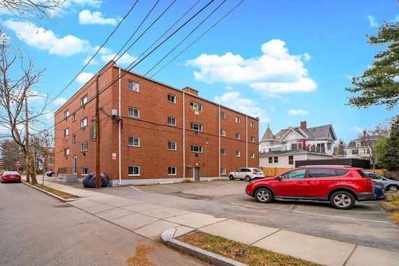 Front view of a multi-story brick apartment building with parking area.
