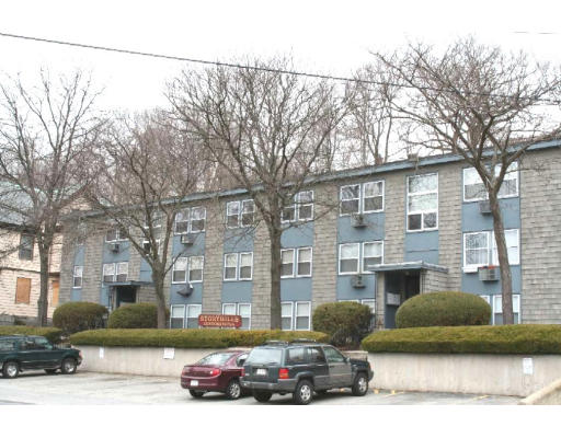 Front view of a three-story apartment building with multiple windows and a parking area in front.