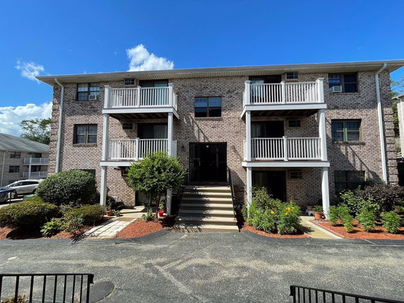 Front view of a three-story brick apartment building with balconies.