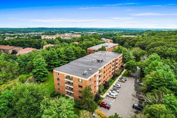 Aerial view of a several-story apartment building surrounded by trees with parking lot.