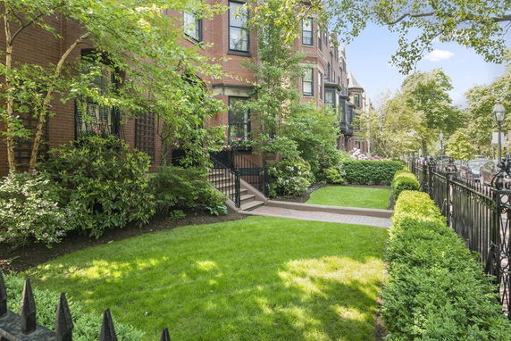 Front view of a row of brick townhouses with a landscaped garden and iron fence.