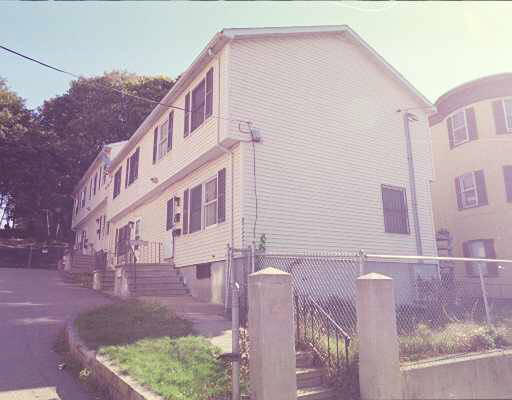 Angled front view of a two-story house with a sloped roof and fenced yard.