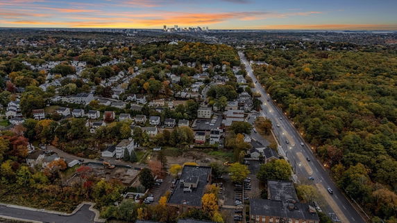 Aerial panoramic view of a residential neighborhood with surrounding greenery and distant city skyline.
