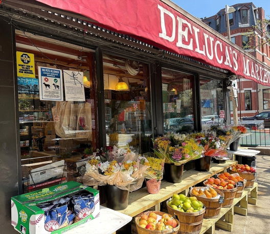 Front view of a market with an awning and various items displayed outside, including flowers and fruit.
