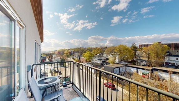 View from a balcony showing a neighborhood with houses and buildings under a blue sky.