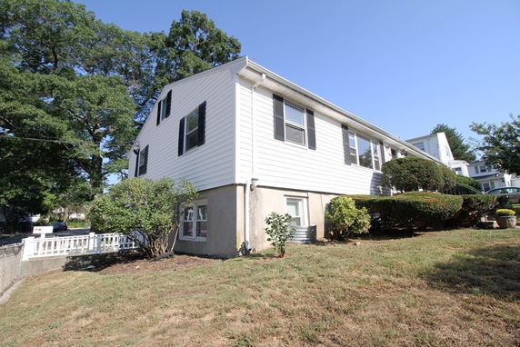 Side view of a two-story house with white siding and black shutters.