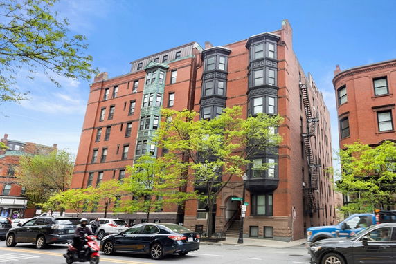 Front view of a multi-story red brick building with bay windows and fire escapes.
