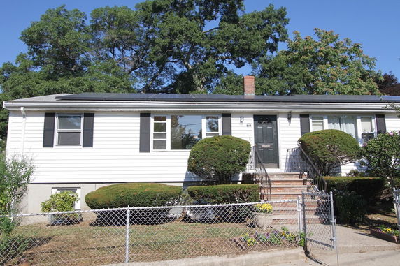 Front view of a single-story house with a black roof and white exterior, featuring a black front door and small bushes in front.