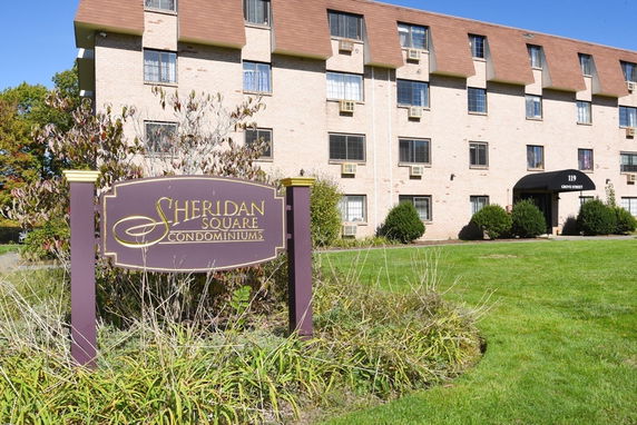 Front view of a residential building with multiple floors and a sign for Sheridan Square Condominiums.