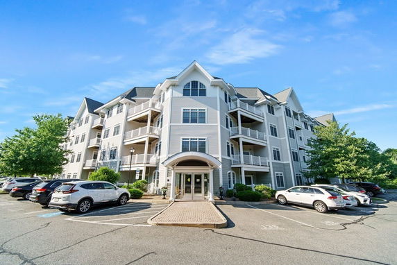 Front view of a multi-story residential building with balconies and a parking area.