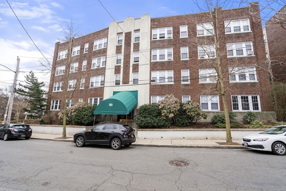 Front view of a four-story brick apartment building with green awning over entrance.