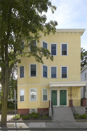 Front view of a three-story yellow house with multiple windows and two green doors.