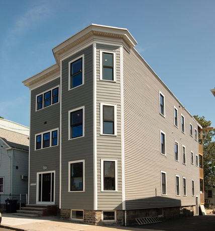Front view of a three-story building with gray siding and multiple windows.