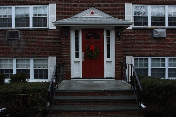 Front view of a brick building with a red door and a small porch.
