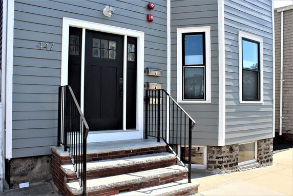Front view of a house with a gray exterior and steps leading to a black door.
