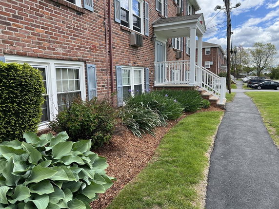 Front view of a two-story brick building with a porch and landscaped garden.