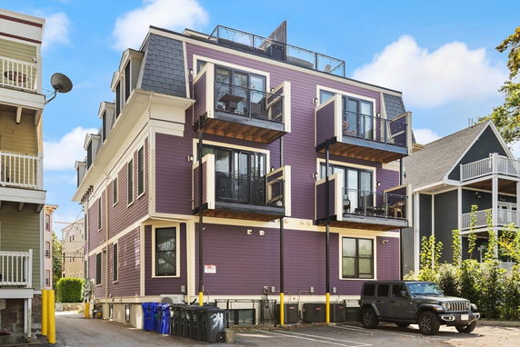 Front view of a multi-story building with balconies and a parking area.