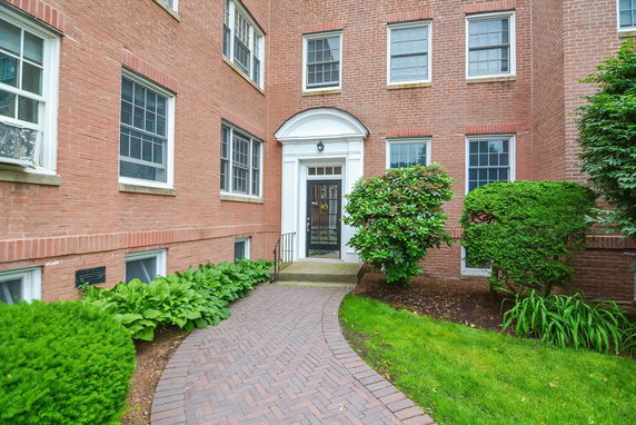 Front view of a brick apartment building with a main entrance door and pathway.