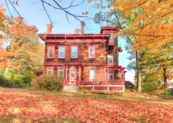 Front view of a multi-story wooden house with autumn foliage.