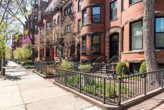 Front view of a row of multi-story brick townhouses with iron railings and small landscaped gardens.