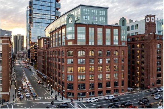 Front view of a multi-story red-brick building located on a busy street corner with modern architecture elements.