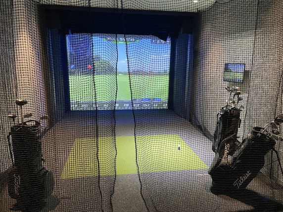 Indoor golf simulator with golf clubs and netting.