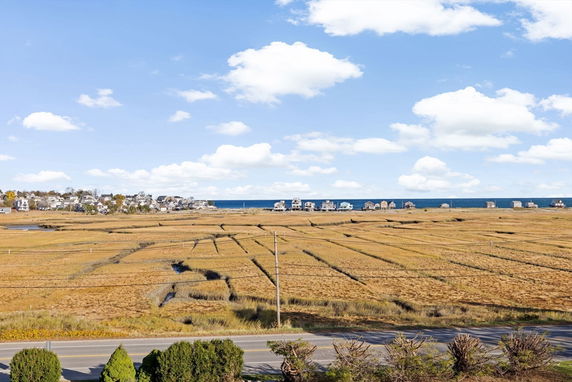 Panoramic view of open fields and houses by the sea.