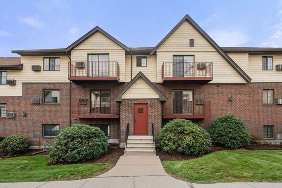 Front view of a multi-story brick apartment building with balconies and a central entrance.