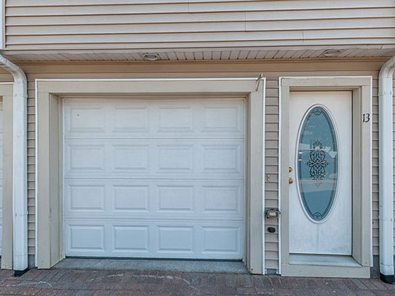 Front view of a house with a single garage door and an entry door with an oval glass panel.