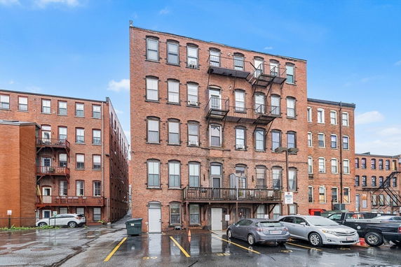 Front view of a multi-story brick building with fire escapes and parking area.