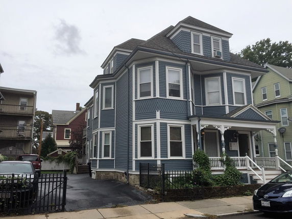 Front view of a multi-story blue house with a pitched roof and bay windows.