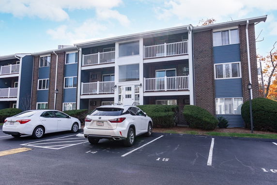 Front view of a multi-story apartment building with balconies and parking area.